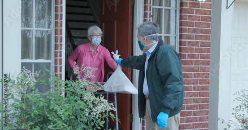 A senior citizen using a walker who is at high risk because of the coronavirus COVID19 gets meals or groceries delivered to her house by a volunteer working with a benevolent organization.