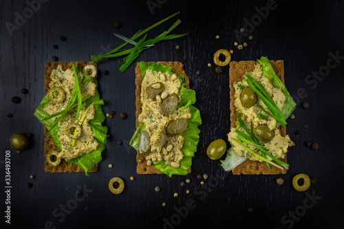 Bread toasts with olives and fresh vegetables on a black background. View from above.