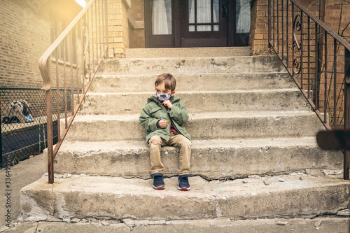 Boy sitting on the front steps with a face mask on during quarantine