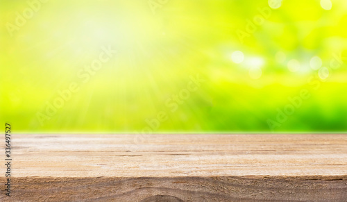 Empty surface of a wooden table on the blurred background of the spring park in sunny day. The surface to display your products. Copy space.