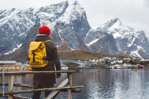 Young man with a backpack standing on a wooden pier the background of snowy mountains and lake. Place for text or advertising