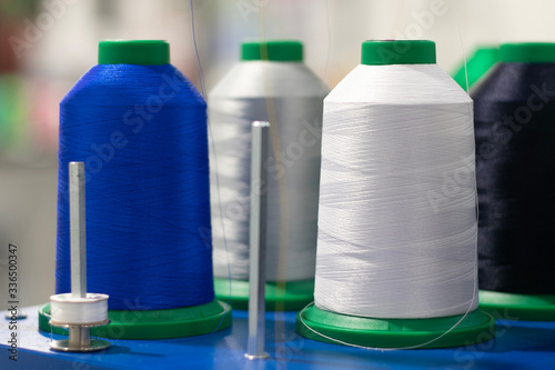 Close up shot of industrial bobbins for fashion industry. Manufacturing concept, dressmaking service, white, blue and black silk supplies. Eastern economy, low cost labor. 