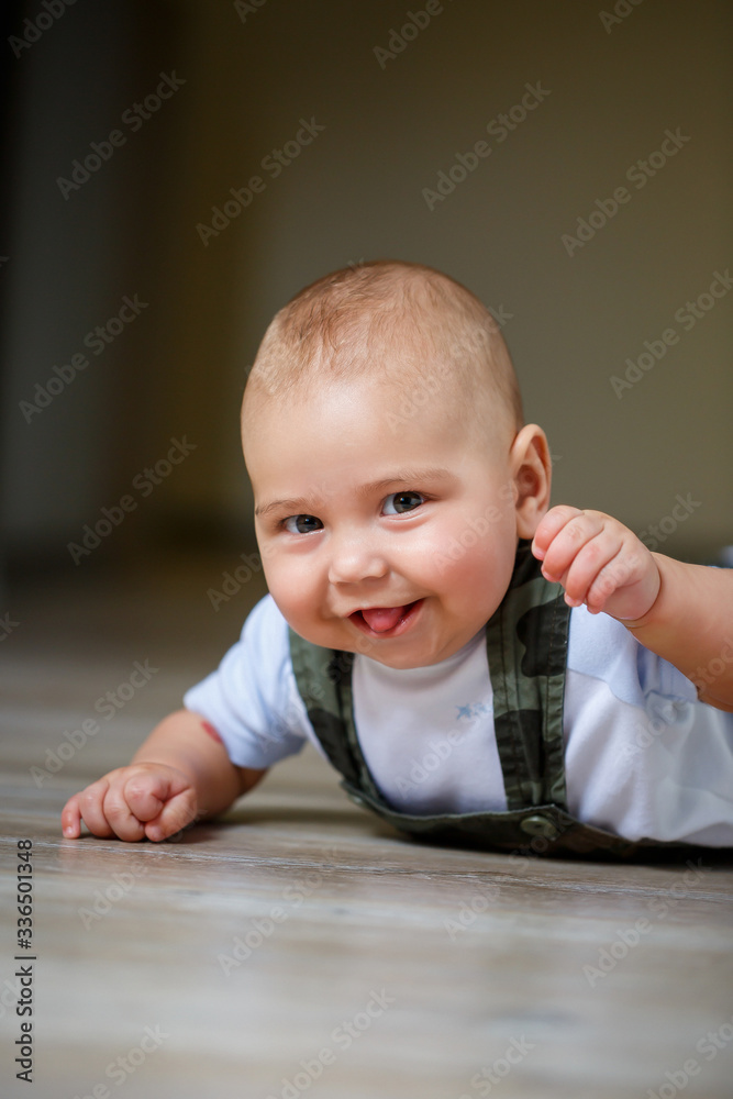 little boy aged 8 months in overalls, a white shirt and white socks crawling on the floor and smiling little boy aged 8 months in overalls, a white shirt and white socks crawling on the floor and smiling