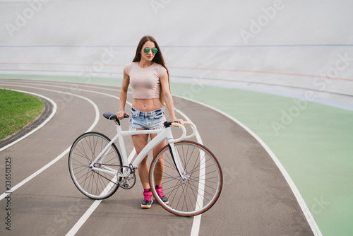 Cycling and fitness. Young beautiful fit woman with perfect body in sportswear with the bike outdoors on the track. Sportive and healthy lifestyle, cyclist working out, training, fashion, beauty.