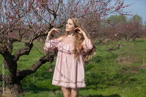 Beautiful blonde woman in pink dress in flowering peach garden in spring
