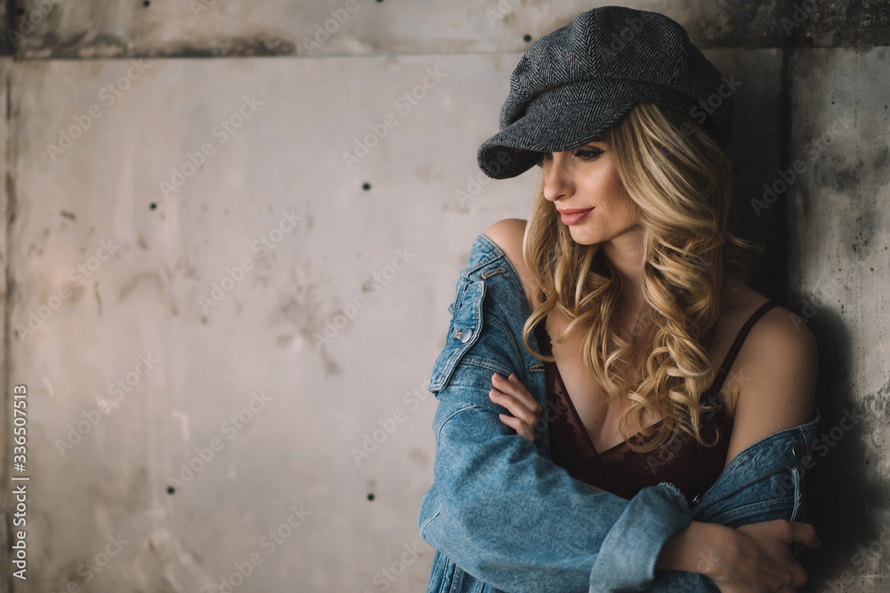 Beautiful sexy woman young  with full lips and curls in a denim jacket and felt cap on a grunge background. Soft selective focus.