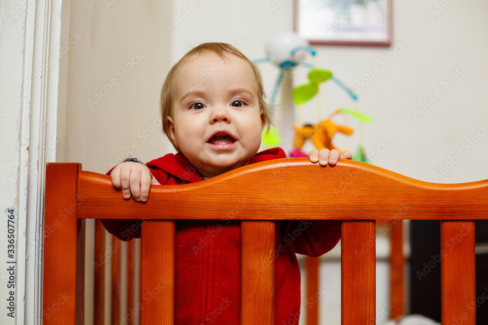 little child girl in a red sweater, smiles beautifully, in a crib, plays and has fun, emotional photo little child girl in a red sweater, smiles beautifully, in a crib, plays and has fun, emotional photo