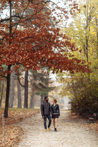 Fototapeta Naklejka Na Ścianę i Meble -  Happy interracial couple walking in autumn park