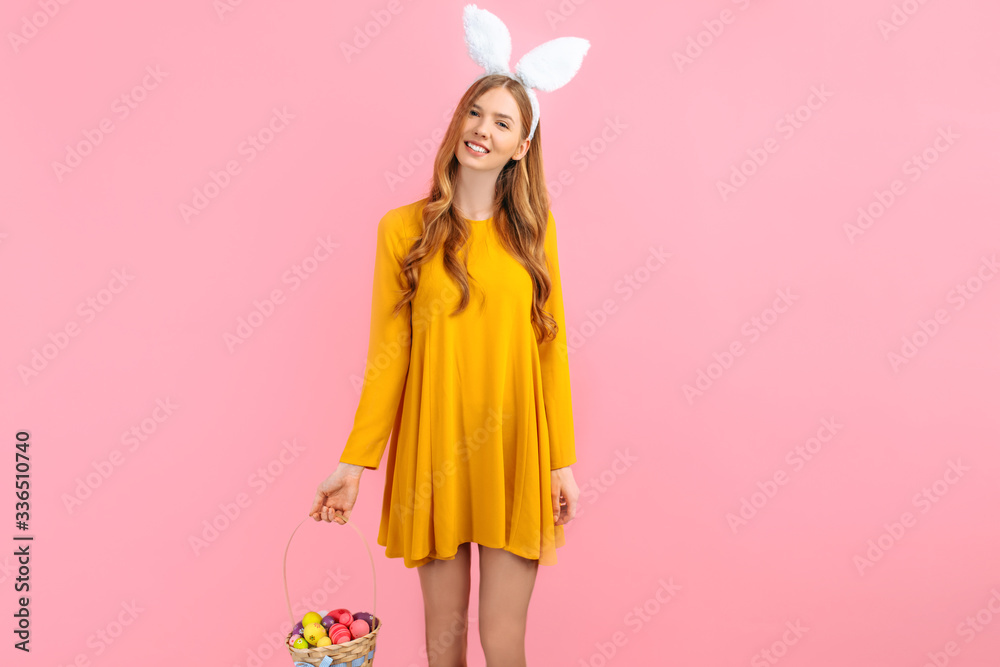 Happy Easter. happy young woman wears rabbit ears on Easter day and holds a basket of Easter eggs, on an isolated pink background Happy Easter. happy young woman wears rabbit ears on Easter day and holds a basket of Easter eggs, on an isolated pink background