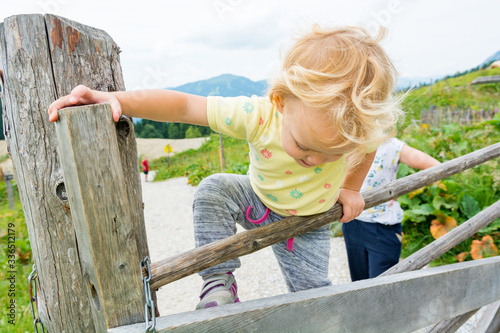 Cute blonde girl climbing across wooden fence on mountain pasture. photo
