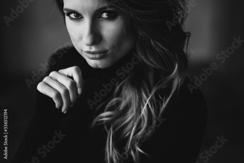 Beautiful woman with curls and full lips in a black turtleneck. Black and white art photo. Soft selective focus.