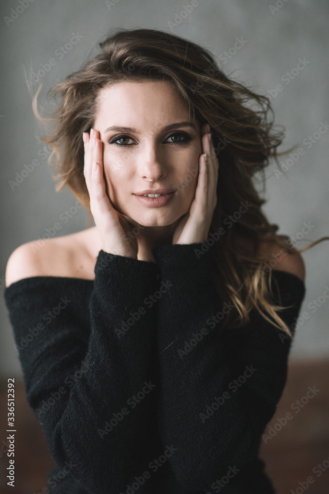 A beautiful woman with curls and full lips in a black sweater holds her face with her hands and looks at the camera. Soft selective focus. A beautiful woman with curls and full lips in a black sweater holds her face with her hands and looks at the camera. Soft selective focus.