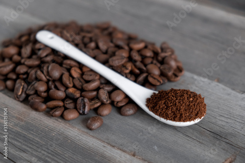  white ceramic spoon with ground coffee on a wooden background Fried Arabica grains