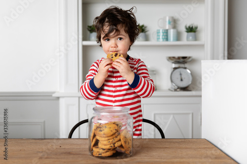 Cute little boy eating a biscuit from cookie jar at kitchen table