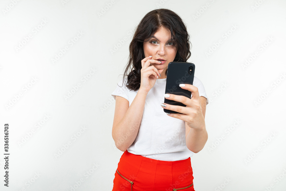 girl in a white T-shirt thoughtfully reads a message on her smartphone on a white studio background with copy space girl in a white T-shirt thoughtfully reads a message on her smartphone on a white studio background with copy space