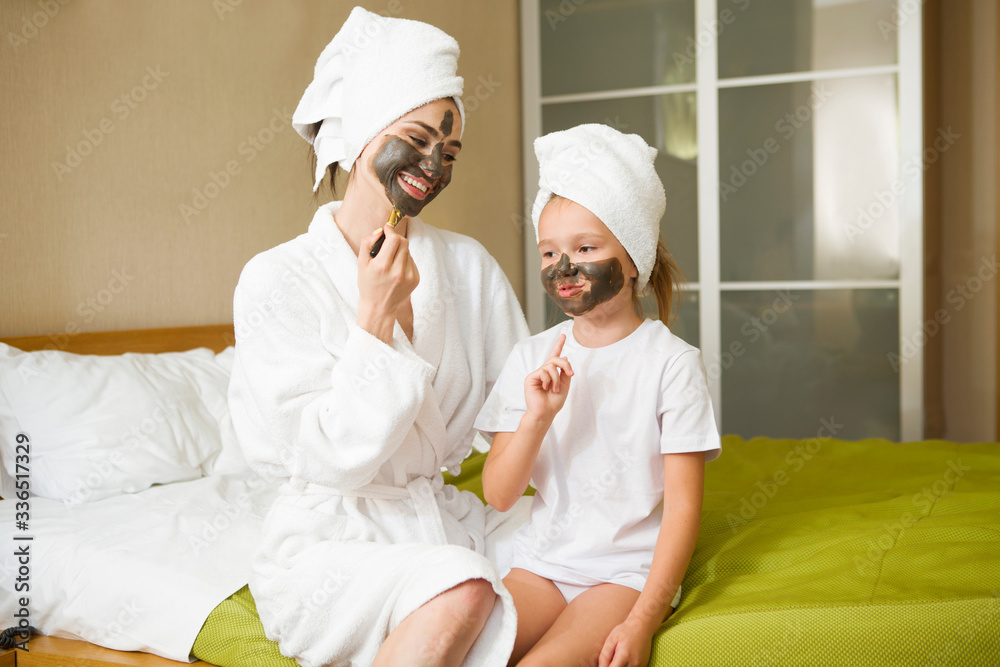 Mom and daughter making clay facial mask at home. Their hair is wrapped in a white bath towel. cheerful time together. chelter in place. Mom and daughter making clay facial mask at home. Their hair is wrapped in a white bath towel. cheerful time together. chelter in place.
