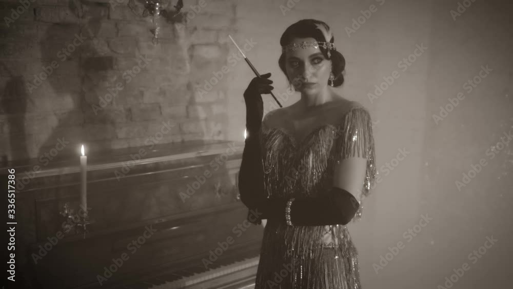  Black, white old-fashioned 30s movie. Portrait young beautiful sexy retro woman. Lady hairstyle finger wave vintage headband. Fashion silver dress. Backdrop room piano romantic bright candles burn
