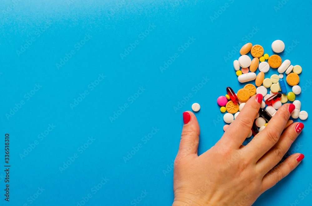 Female hand taking multi-colored pills lying on a blue background. Female hand taking multi-colored pills lying on a blue background.
