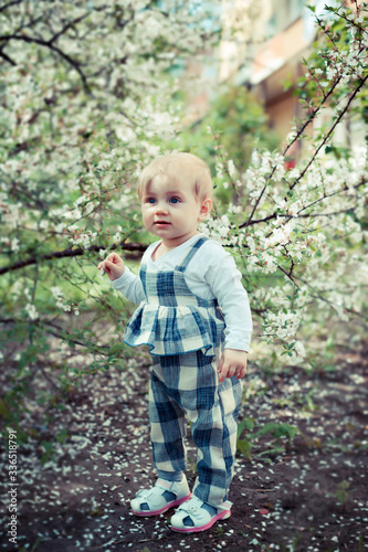 little one-year-old girl walking in spring garden.