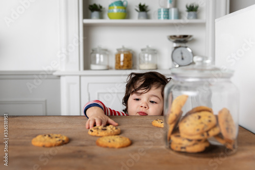Young boy reaching at cookies on kitchen table