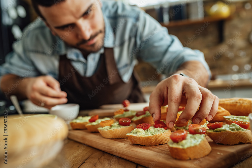 Close-up of man preparing bruschetta with healthy ingredients.