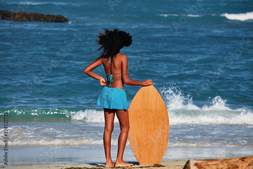 Young curly-haired girl with a surfboard on the beach. Water sport activity, Atlantic Ocean © Baranov