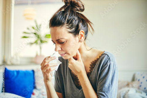 Sick woman with pain in throat sitting in bed with high fever.