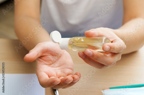 Young man applying sanitizer gel on his hands while sitting at his working table in office