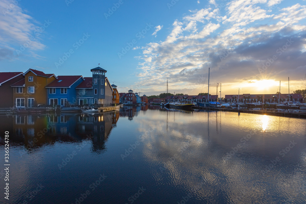 Netherland, Groningen - colorful wooden houses
built on canals, illuminated by the morning paparsky sun with boat dock.