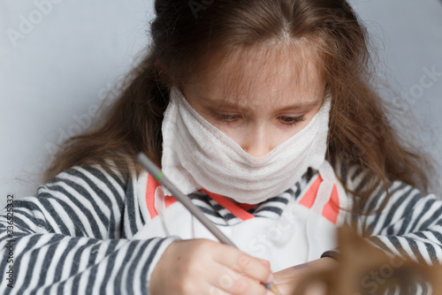 ute little caucasian child girl wearing a protective mask and draws in pencil at a table in a child's room