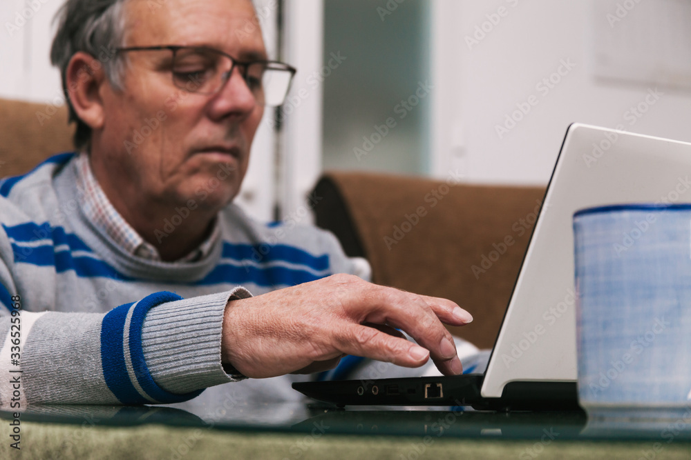 Senior man using a computer at home. Telecommuting during quarantine. Communication with family members during confinement. Selective focus. Senior man using a computer at home. Telecommuting during quarantine. Communication with family members during confinement. Selective focus.