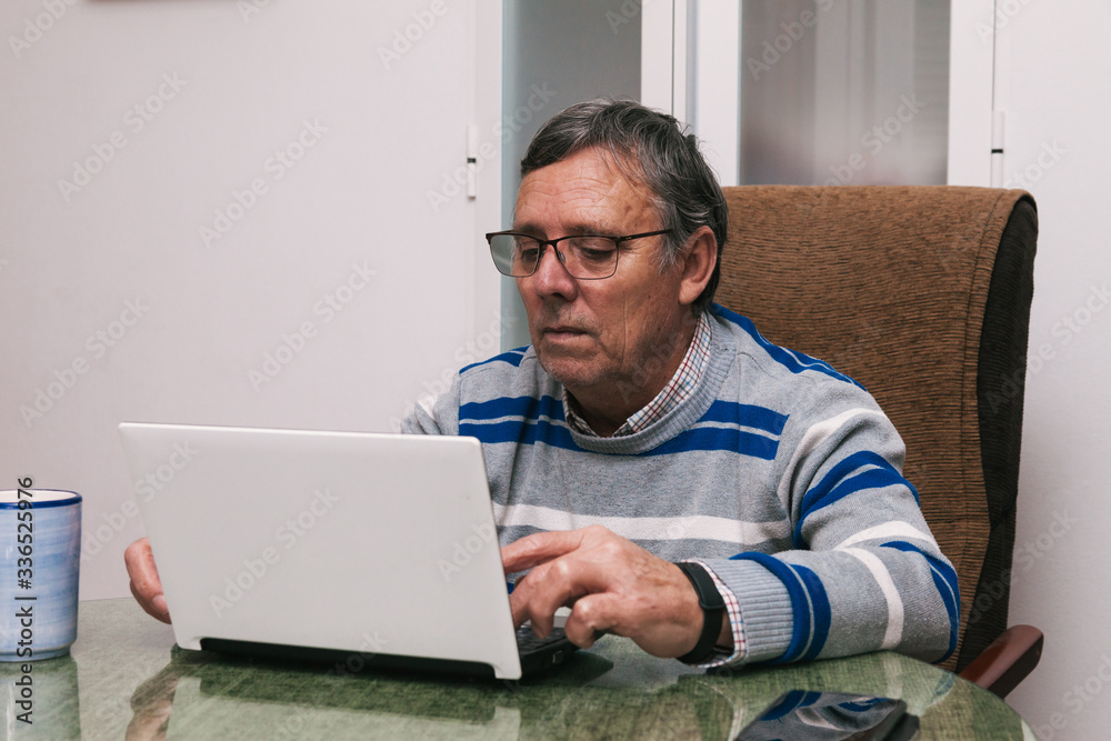 Senior man using a computer at home. Telecommuting during quarantine. Communication with family members during confinement. Selective focus. Senior man using a computer at home. Telecommuting during quarantine. Communication with family members during confinement. Selective focus.