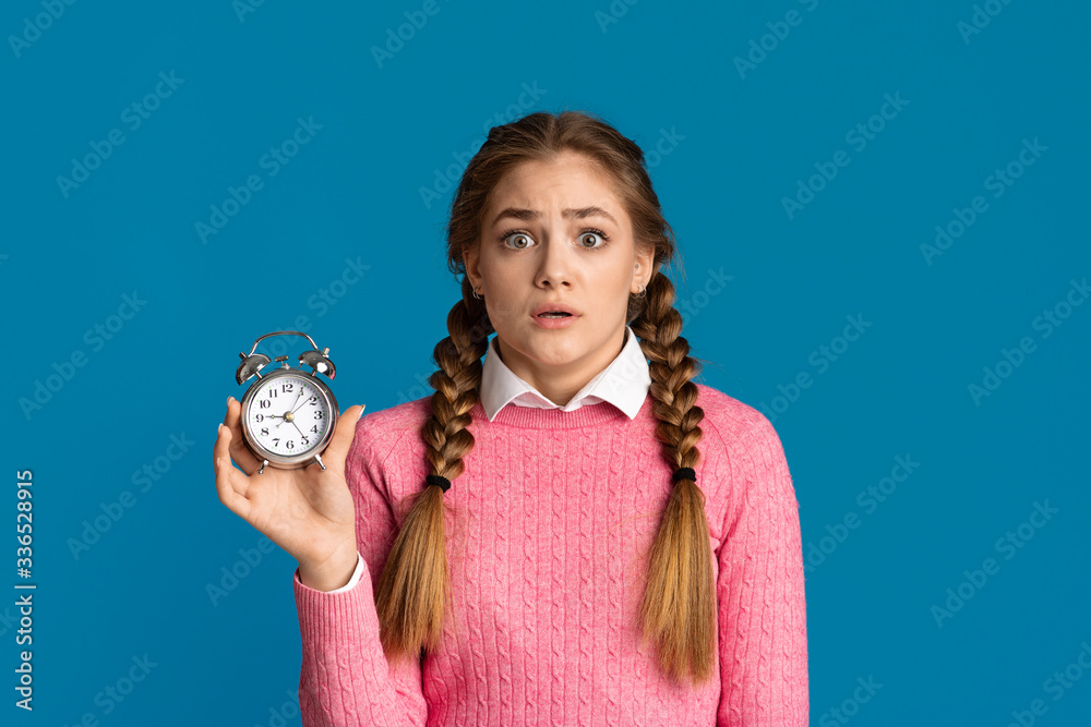 Frightened girl holding alarm clock in hand Frightened girl holding alarm clock in hand