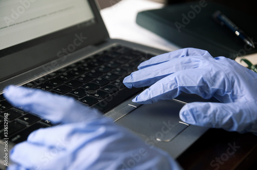 Working on a laptop in disposable gloves - pandemics precaution concept photo