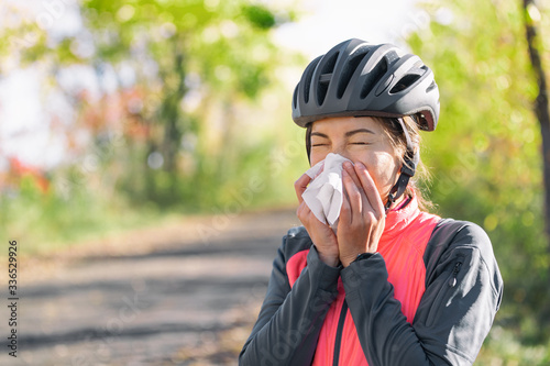 Cough in tissue covering nose and mouth when coughing outside as COVID-19 hygiene guidelines for Coronavirus spread prevention. Biking cyclist girl sneezing in paper outside. photo
