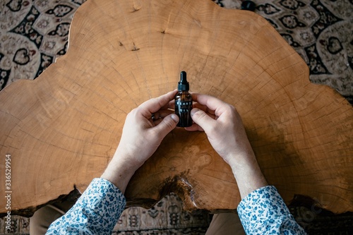 Man holding beard oil bottle on live edge wood table