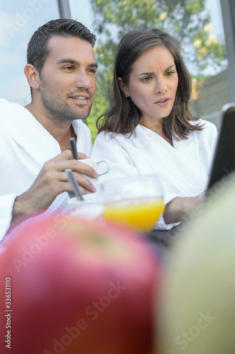 Happy young couple in bathrobes are surfing on the web outdoors