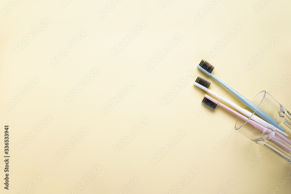 Multi-colored toothbrushes in a glass cup on a yellow background with space for text, flat lay. Multi-colored toothbrushes in a glass cup on a yellow background with space for text, flat lay.