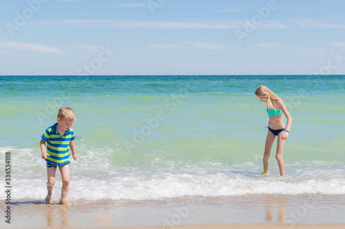 Brother and sister on the beach, the ocean. A teenage girl and a little boy are walking along the coast.