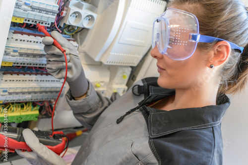 Woman electrician tests circuit breakers in a electrical panel
