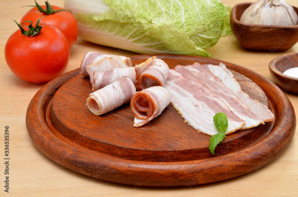 sliced ​​bacon on a wooden board and vegetables on the table