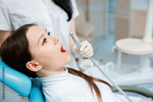 Patient in dental chair. Dentist s hands with gloves work with a dental tools. Beautiful young woman having dental treatment at dentist s office.
