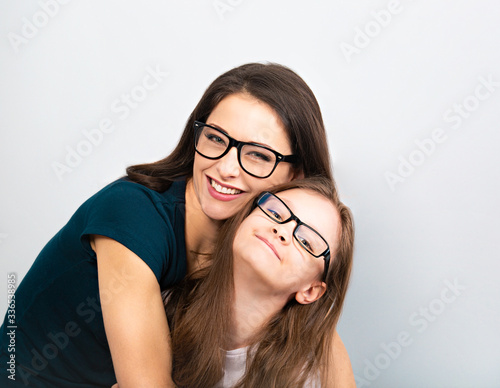 Young casual toothy smiling mother and happy kid in glasses hugging on light blue background. Closeup studio portrait. Teaching kids staying at home. Online education.