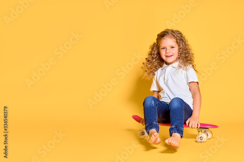 Active and happy girl with curly hair, headphones having fun with penny board, smiling face stand skateboard. Penny board cute skateboard for girls. Lets ride. Girl with penny board yellow background.