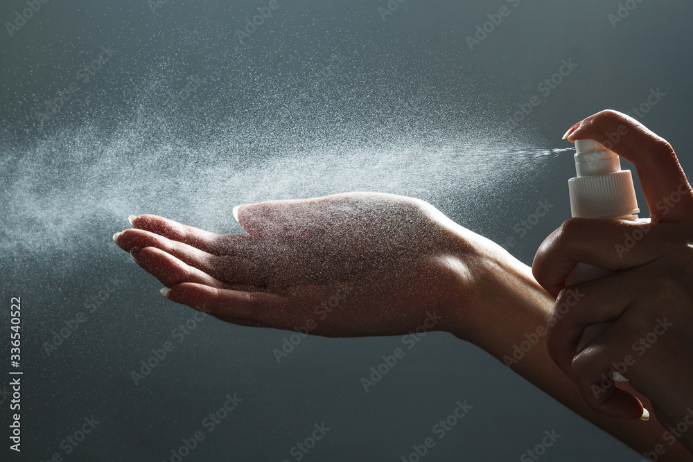 Close-up view of human hand and antiseptic spray bottle on dark background. Sanitation of hands. Control Epidemic Prevention measures of coronavirus. - obrazy, fototapety, plakaty 