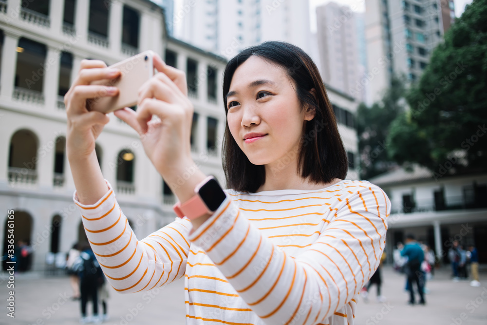Charming Asian woman taking selfie on background of buildings
