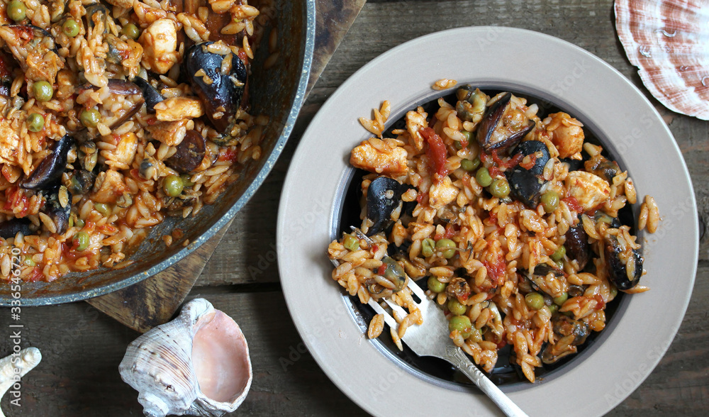 orzo pasta with mussels, seashells and chicken. Seafood paella, traditional spanish dish. Paella on rustic black wooden table. Top view orzo pasta with mussels, seashells and chicken. Seafood paella, traditional spanish dish. Paella on rustic black wooden table. Top view