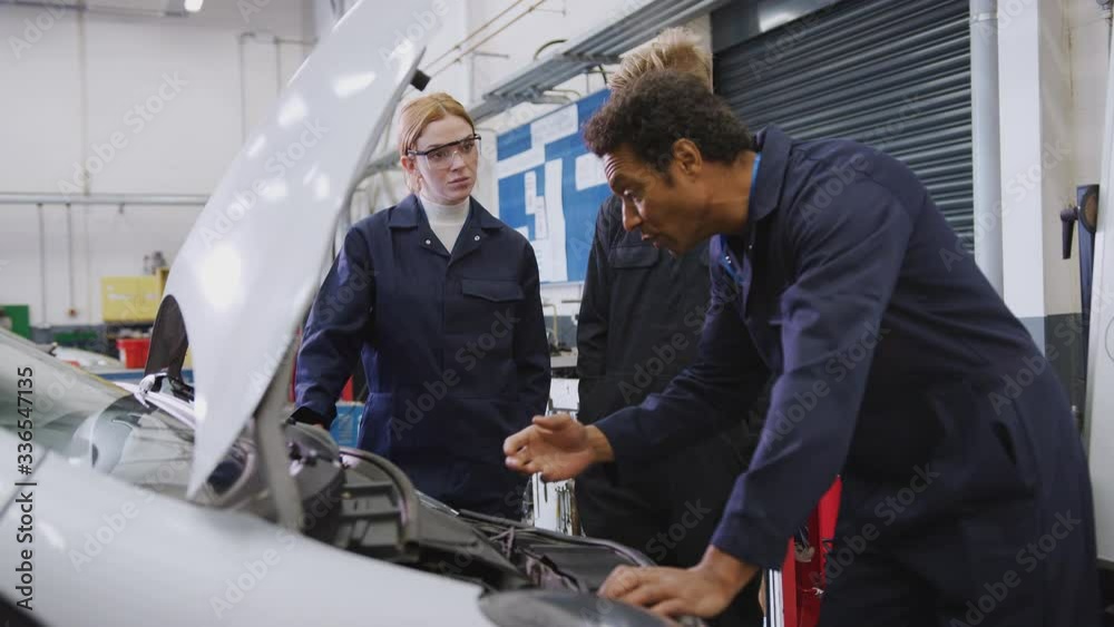Male tutor looking at car engine with students studying auto mechanic apprenticeship at college - shot in slow motion Male tutor looking at car engine with students studying auto mechanic apprenticeship at college - shot in slow motion