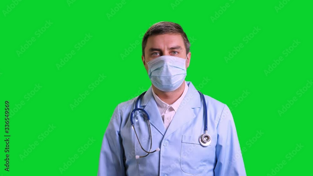 Young doctor stand and looking into camera. Man in blue medical uniform with stethoscope on green chroma key background Young doctor stand and looking into camera. Man in blue medical uniform with stethoscope on green chroma key background