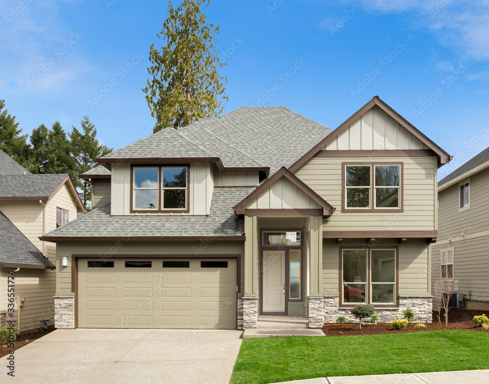 Exterior of new home on bright sunny day with blue sky.  Design features gables and covered porch. Has large two car garage and green lawn.